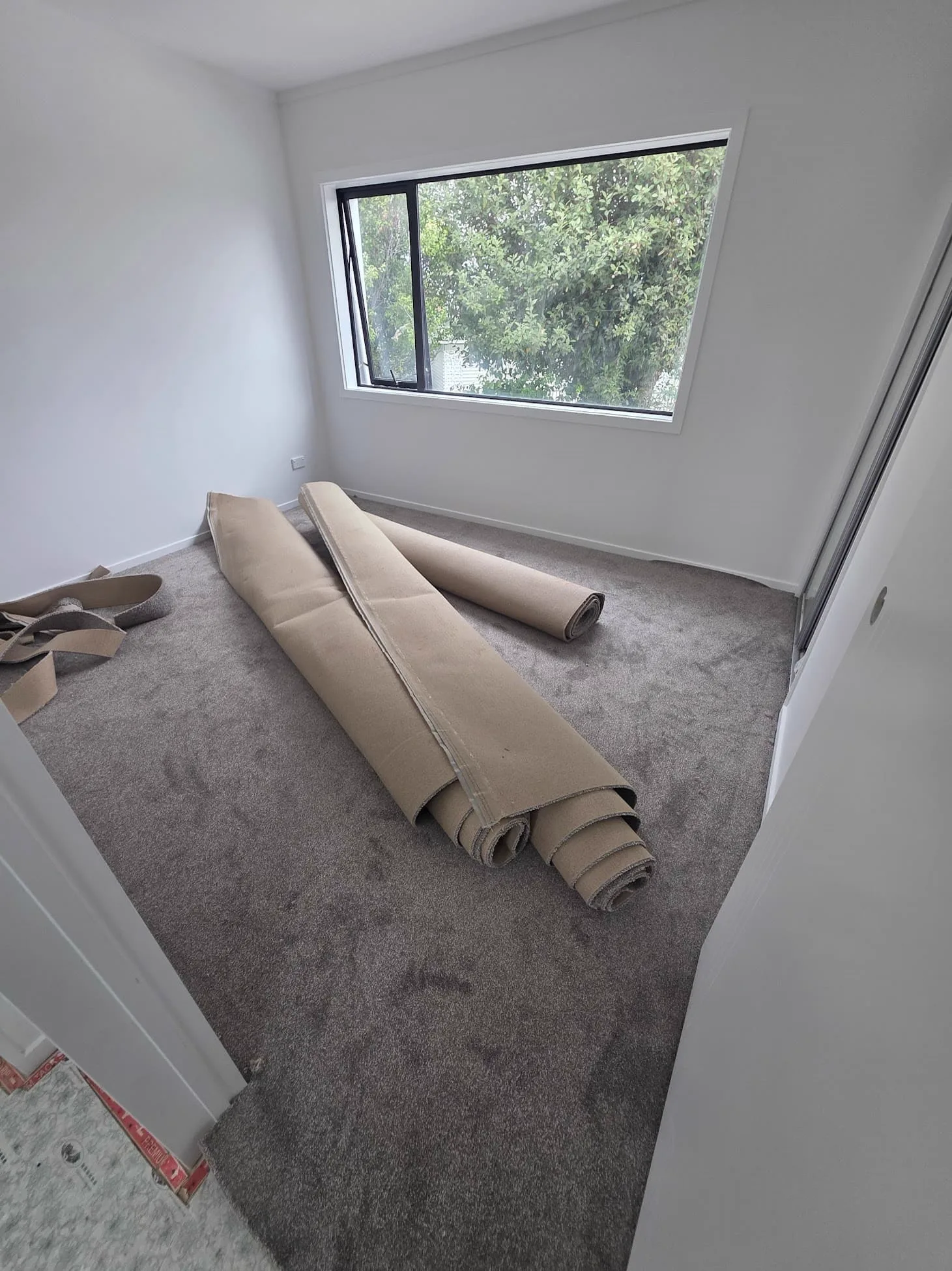 A bedroom part way through a carpet install, with grey carpet laid and offcuts still rolled up on the floor
