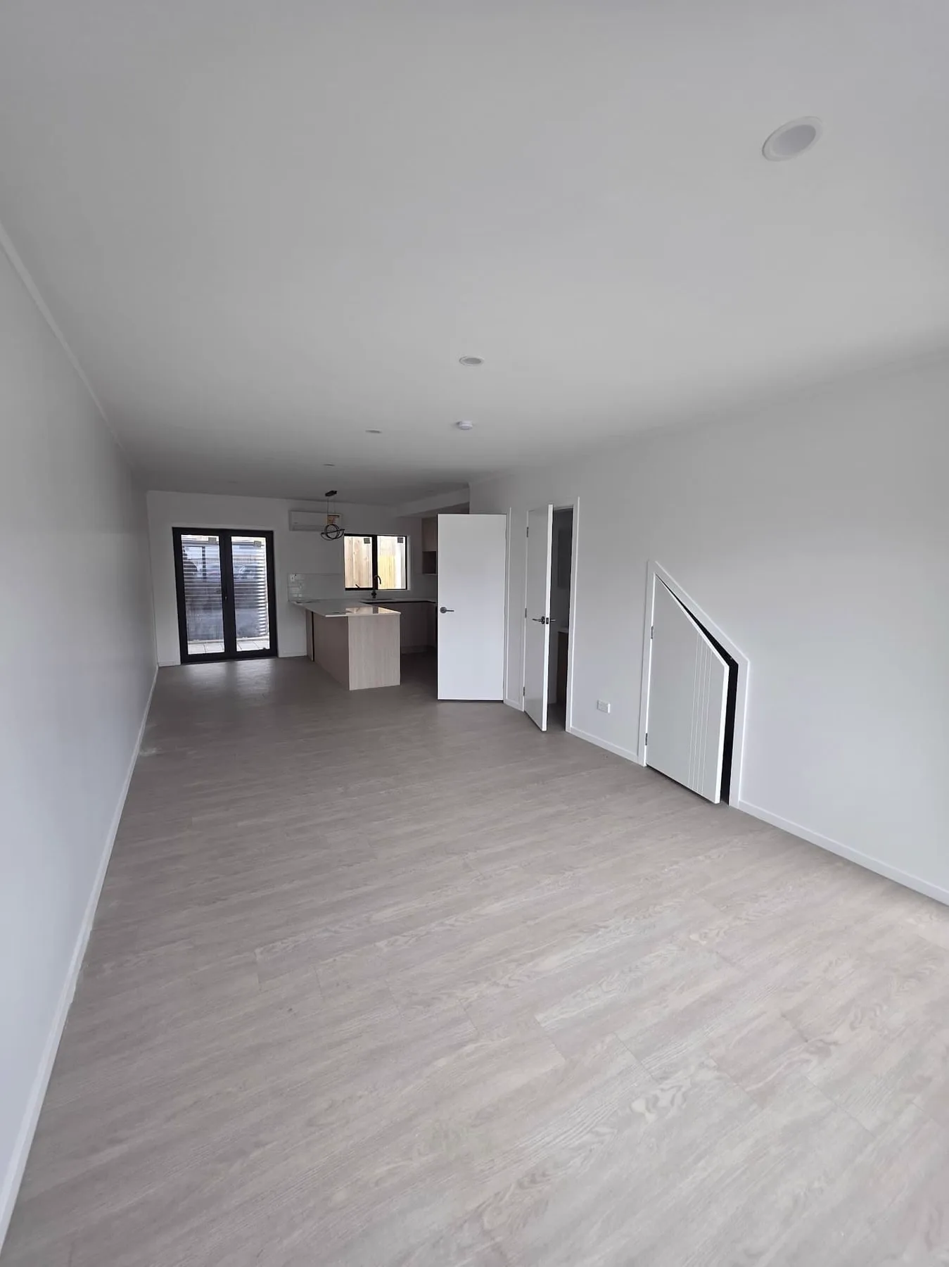 Open plan living room and kitchen with light grey plank flooring running unbroken through to the kitchen, no transition strip at the doorway