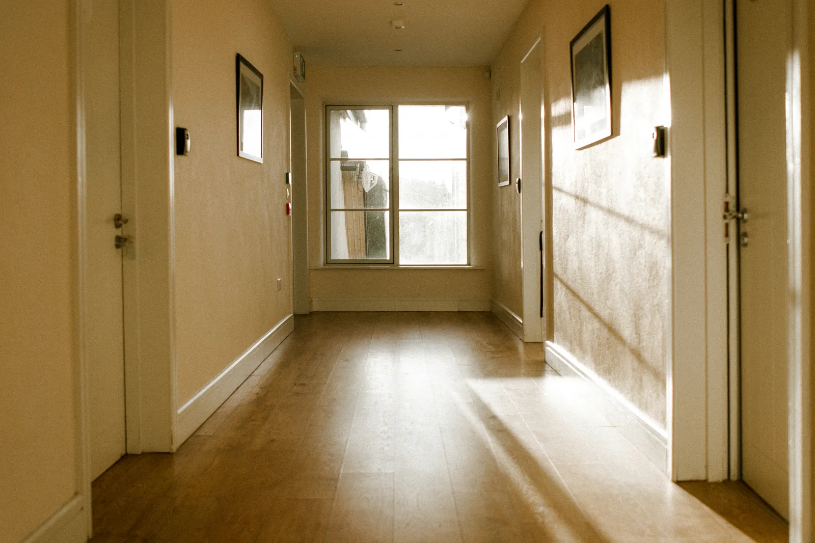 Sunlit hallway with warm timber look plank flooring running between doorways to a window at the end