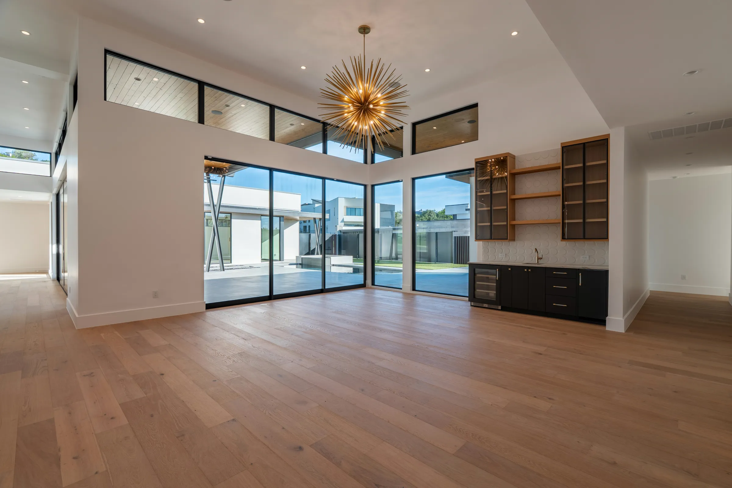 Spacious empty living area with light oak plank flooring, tall windows and a high ceiling