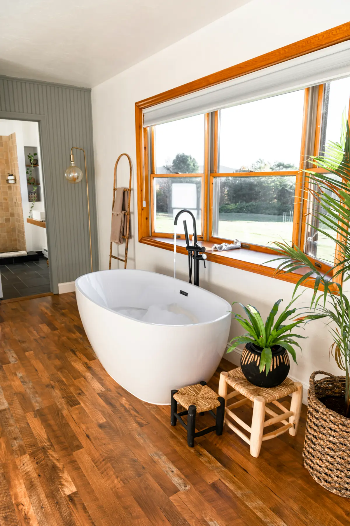 Freestanding bathtub in a bathroom with warm wide plank wood-look flooring and a large window