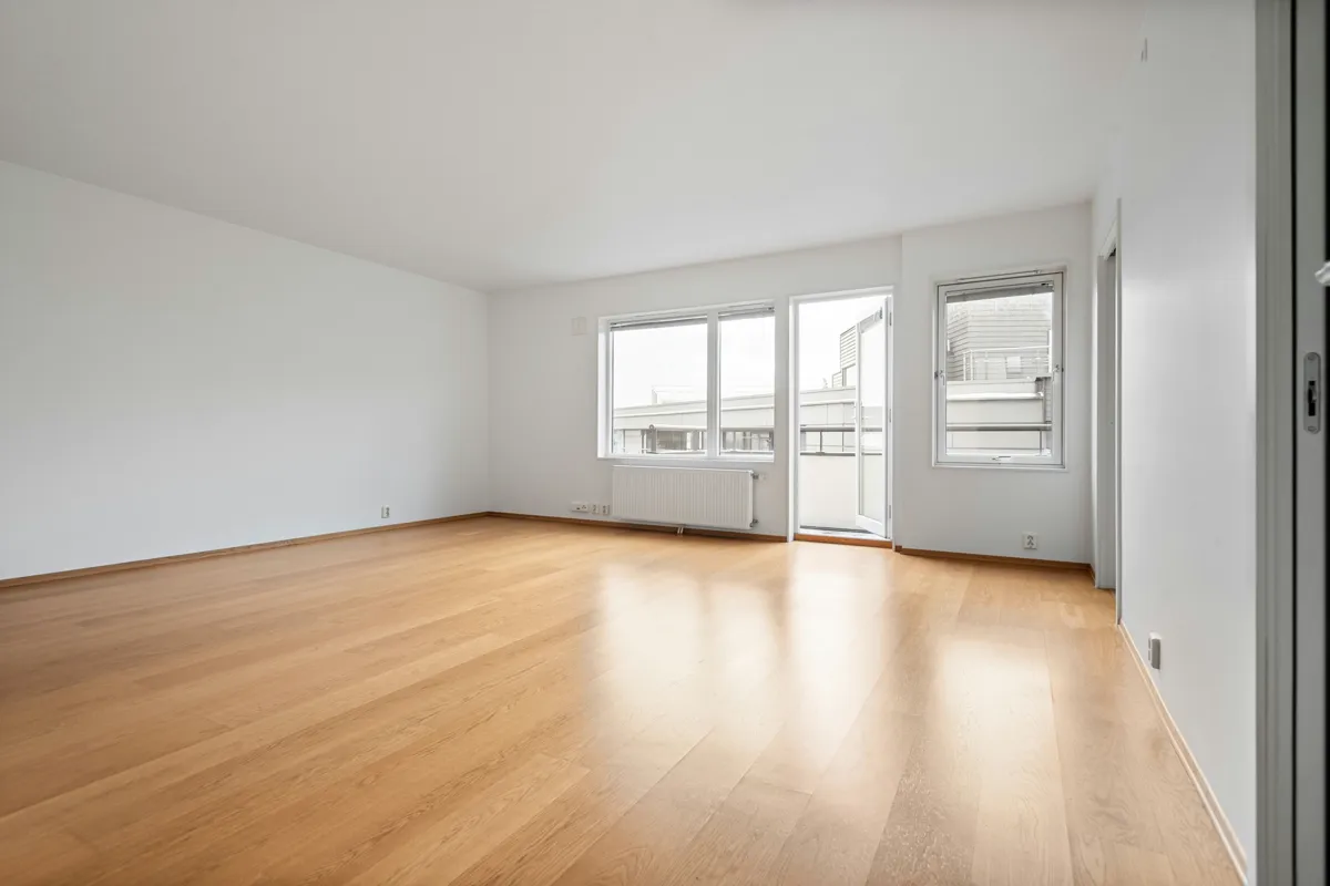 Bright empty living room with light oak plank flooring, tall windows and a glass door to a balcony